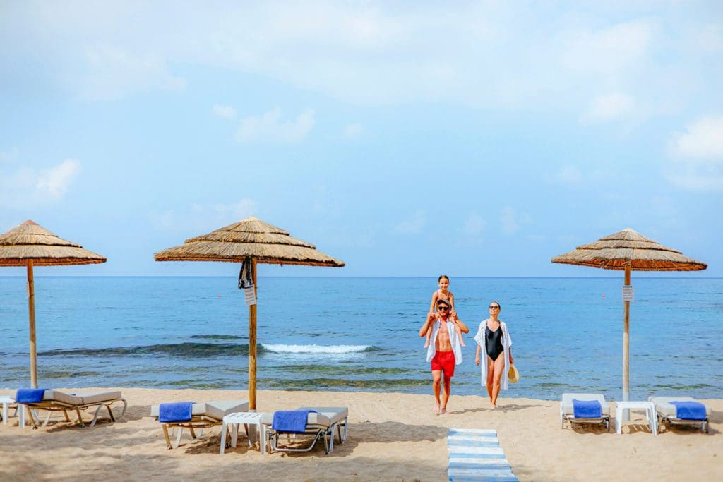 A family walks together across a beach near the ocean while staying at Louis Ledra Beach Resort, one of the best all-inclusive resorts in Cyprus for families.