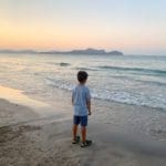 A young boy looks out onto the ocean near Mallorca at sunset.