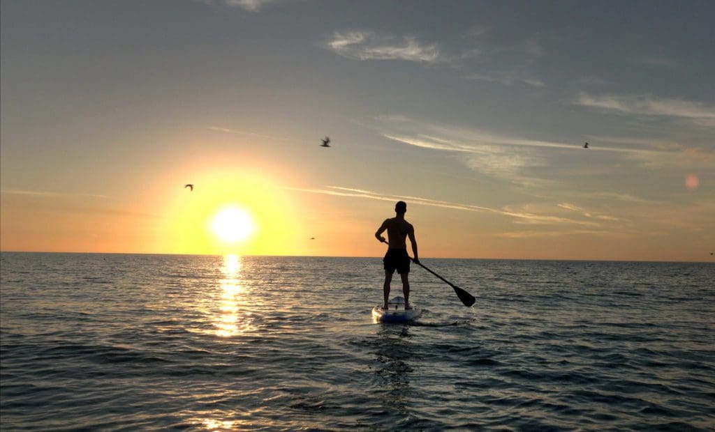 A man paddleboards in the ocean off-shore from Anna-Maria Island at sunset.