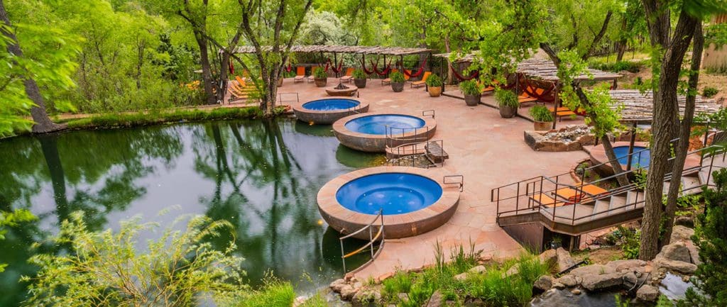 An aerial view of the thermal pools near a lush pond area at Ojo Santa Fe Spa Resort, one of the best hotels for a spa weekend getaway.