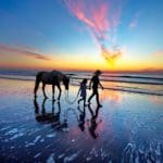 Mother and daughter walking a horse on the beach at sunset on Amelia Island.