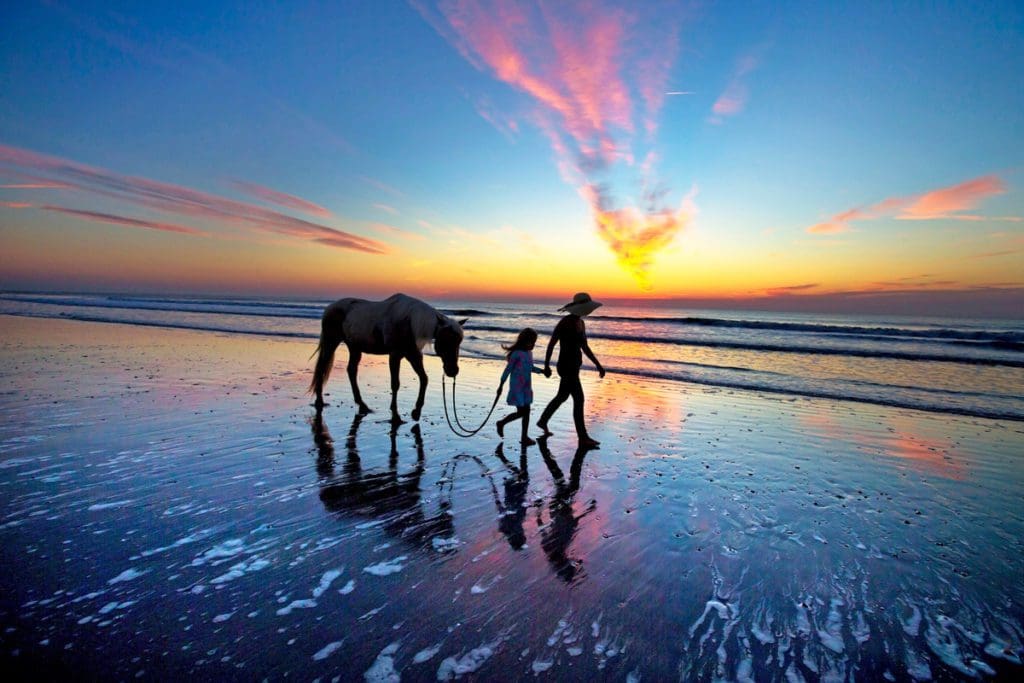 Mother and daughter walking a horse on the beach at sunset on Amelia Island, one of the best beach towns on the East Coast with kids.