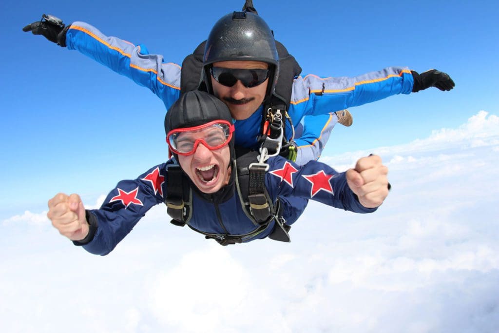 Two men tandem skydive amongst the clouds, one of the best extreme sports to do with teens on a family trip.