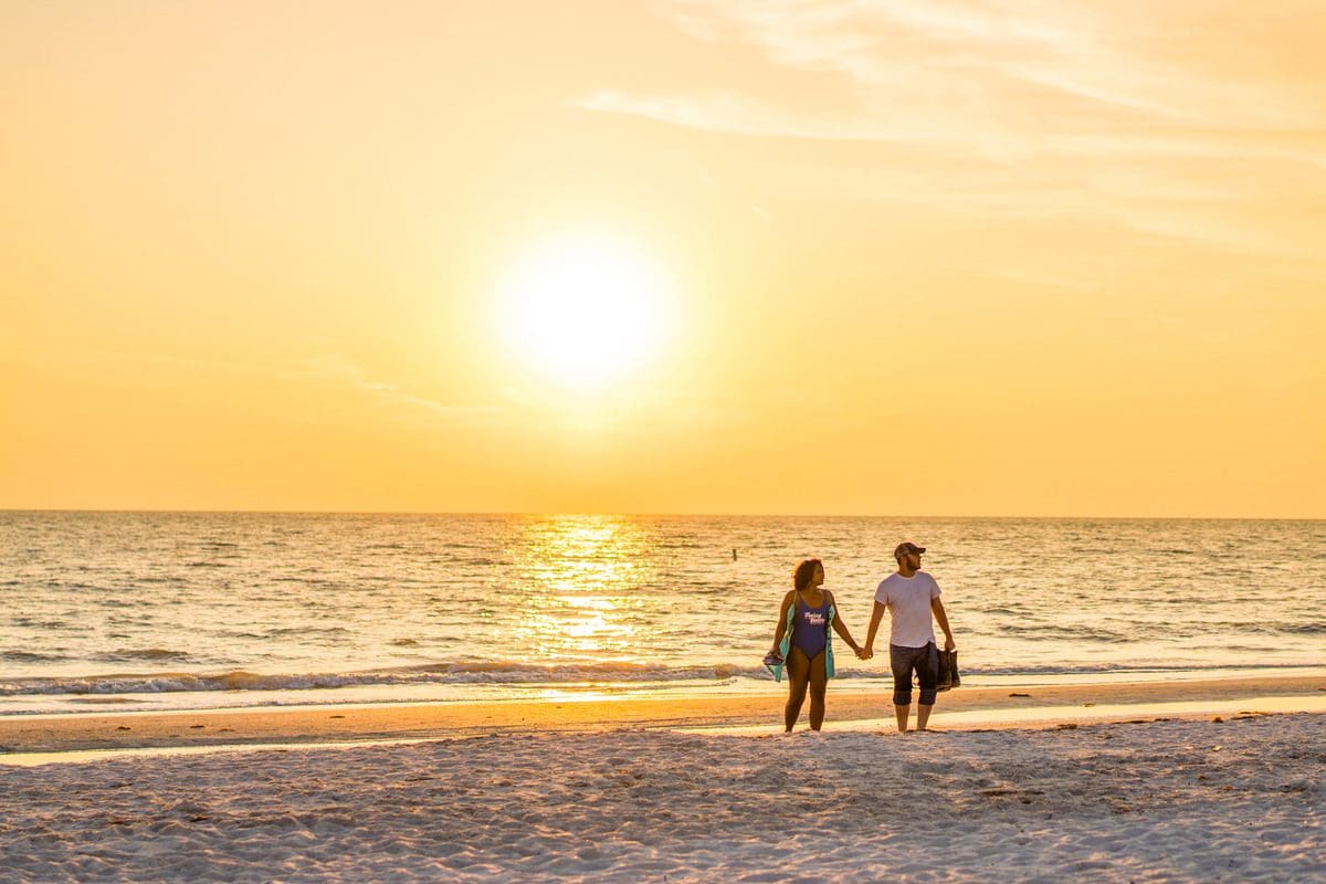 A couple walks hand-in-hand along the St. Pete Beach at sunset.