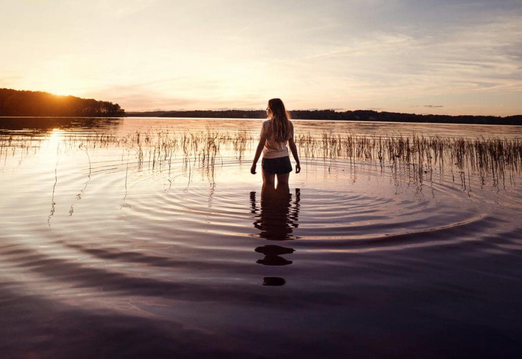 A young woman stands in the waters of Badin Lake, one of the best lakes in North Carolina for a family vacation, at sunset.