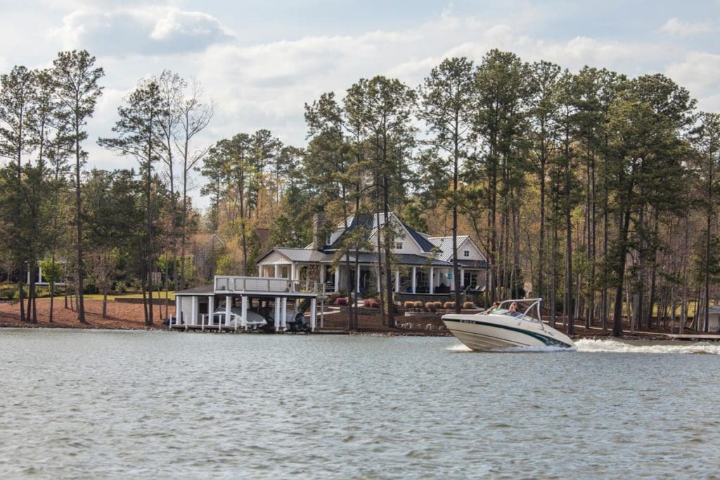 A boat zooms past a lovely house nestled on the shores of Lake Gaston, one of the best lakes in North Carolina for a family vacation.