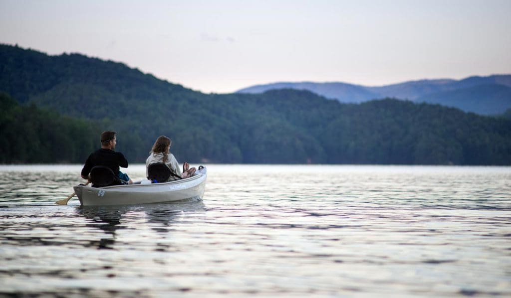 Two people canoe across Lake James with mountains in the distance.