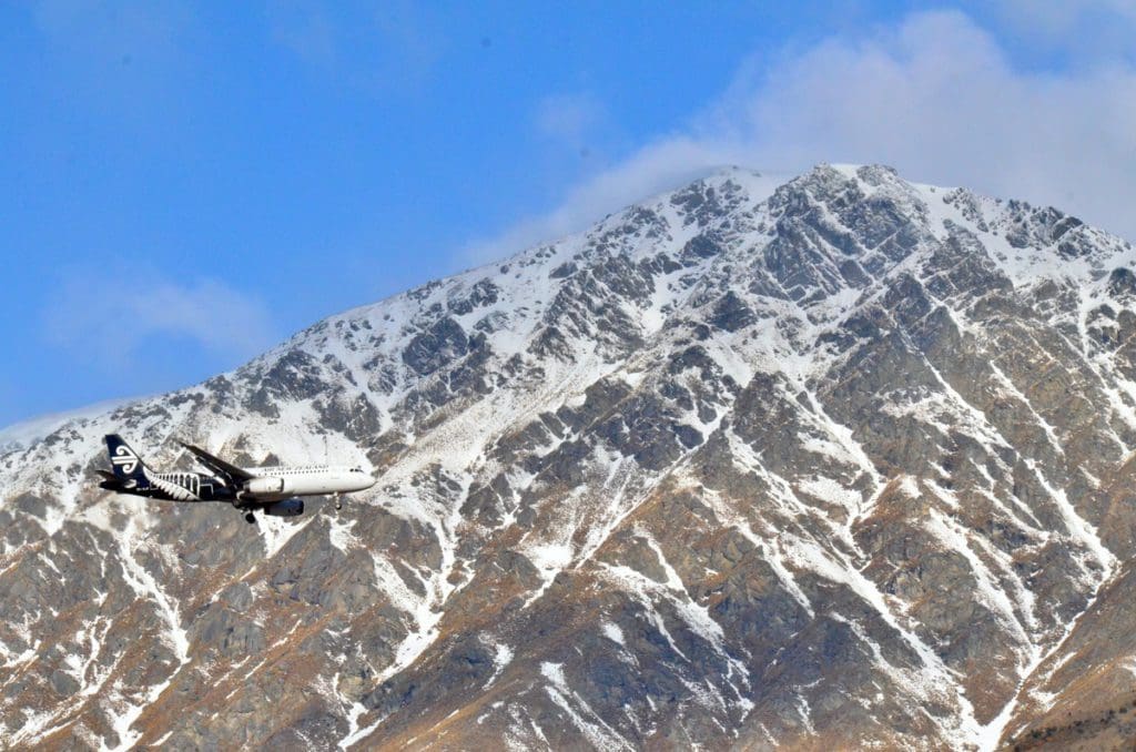 An Air New Zealand plane flies passed a snowy mountain.