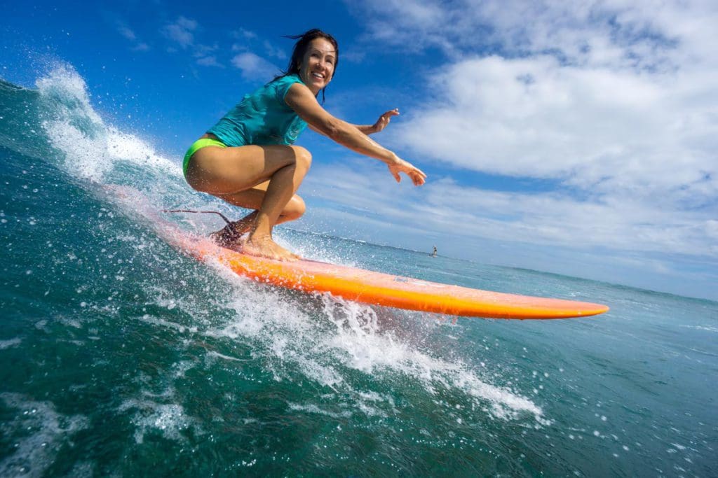 A teen girl on a surf board catching a wave, one of the best extreme sports to do with teens on a family trip.