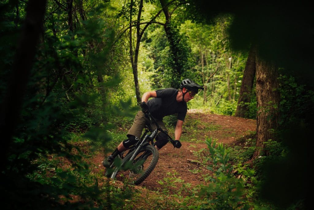 A teen boy races through a wooded path on a mountain bike, one of the best extreme sports to do with teens on a family trip.