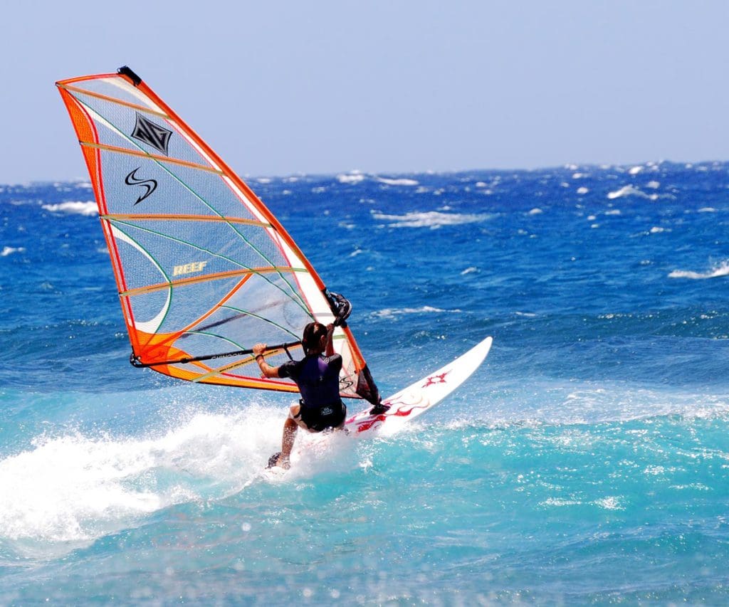 A teen girl windsurfs amongst the ocean surf.