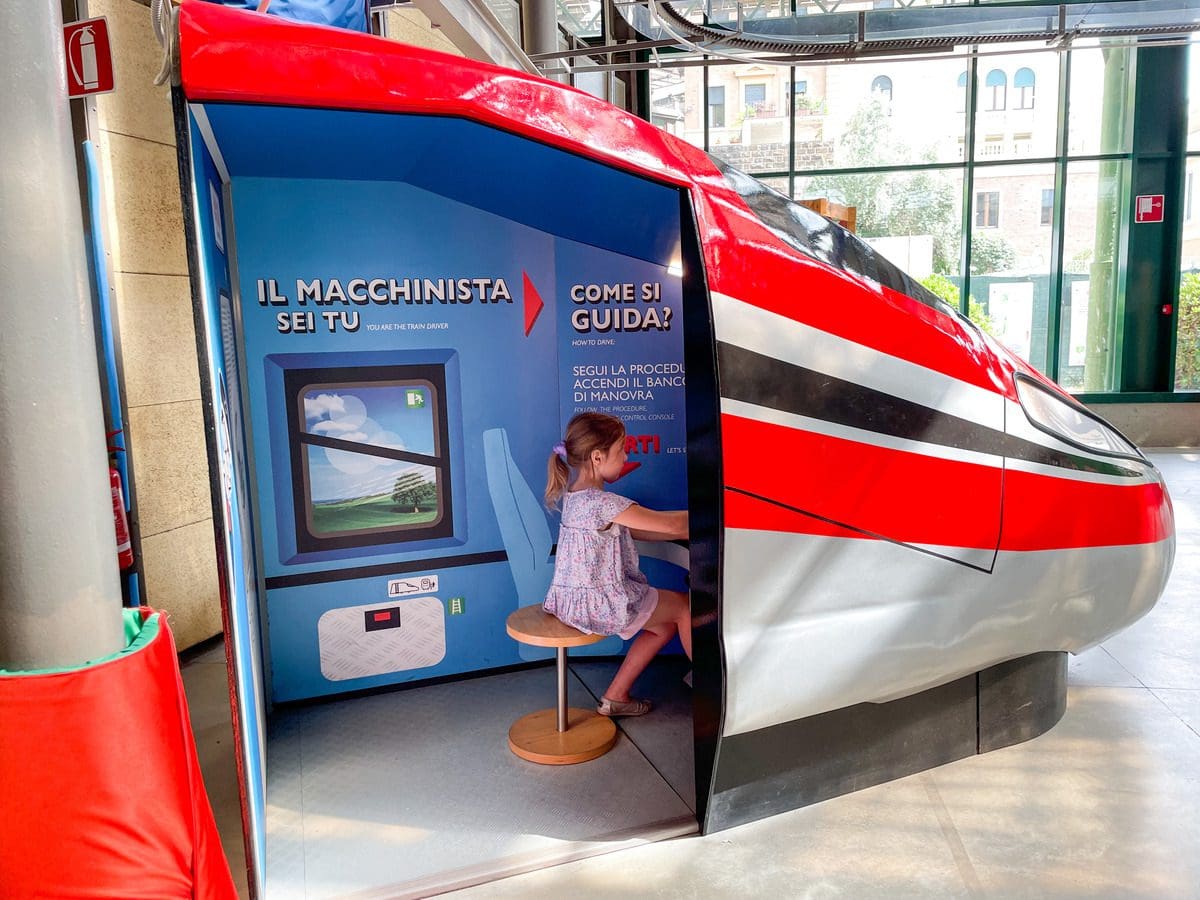 A young girl pretends to drive an Italian train, while visiting Explora il Museo dei Bambini di Roma, one of the best museums in Rome with kids.