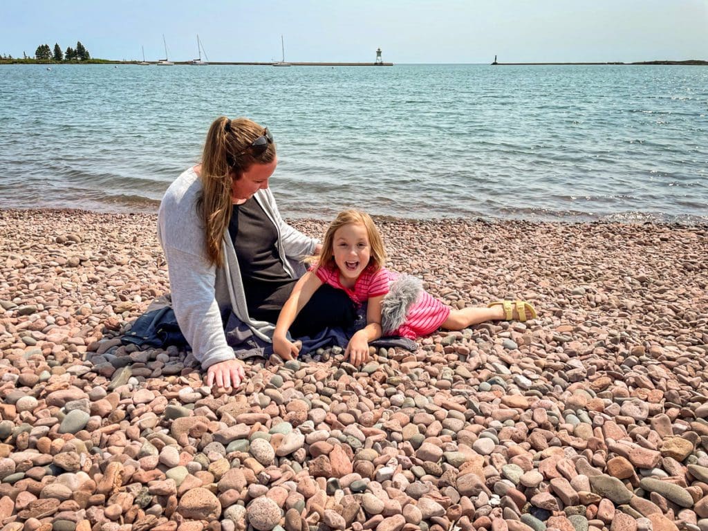 A young girl and her mom sit on a rocky beach along Lake Superior.