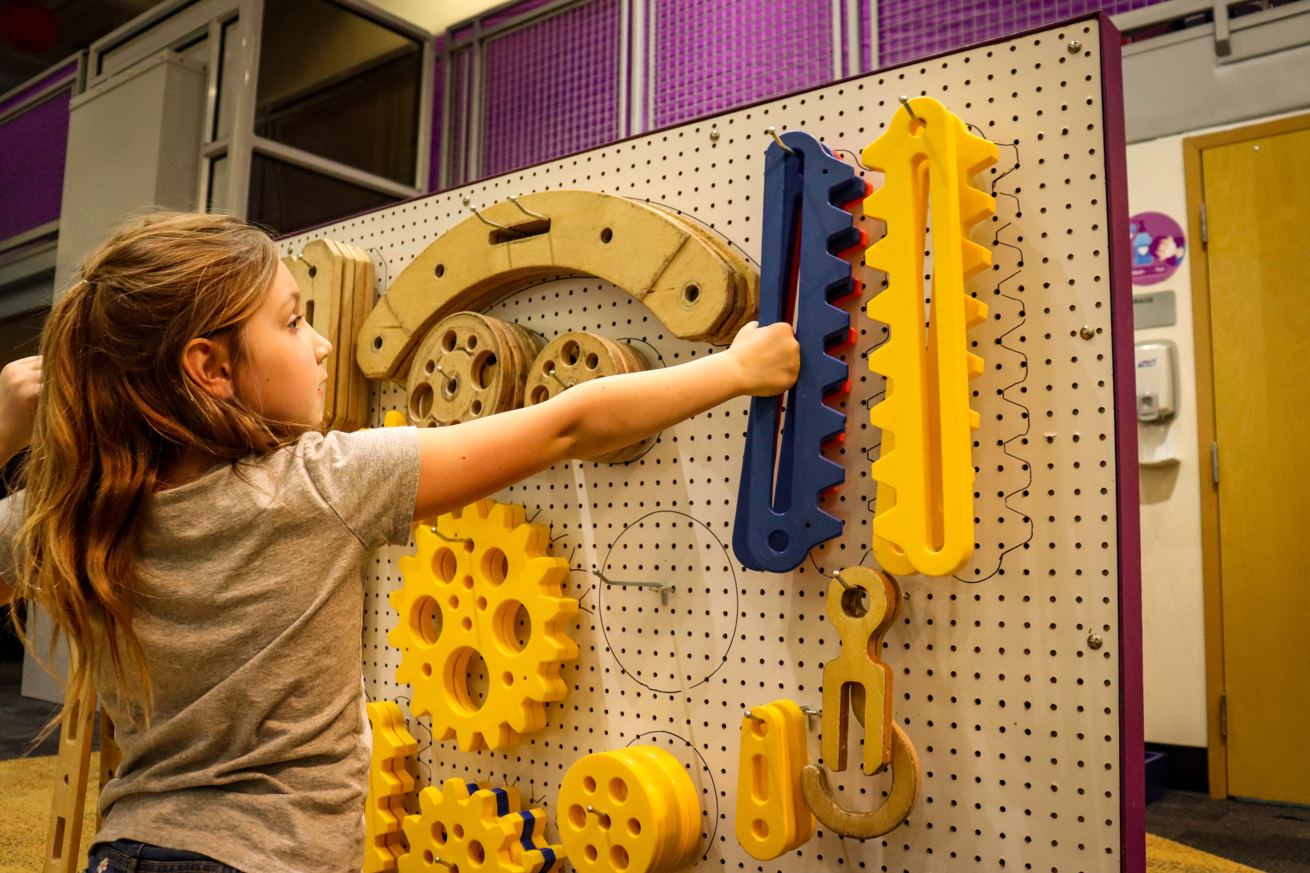A young girl reaches for tools at an engineer exhibit at Glazer Children's Museum.