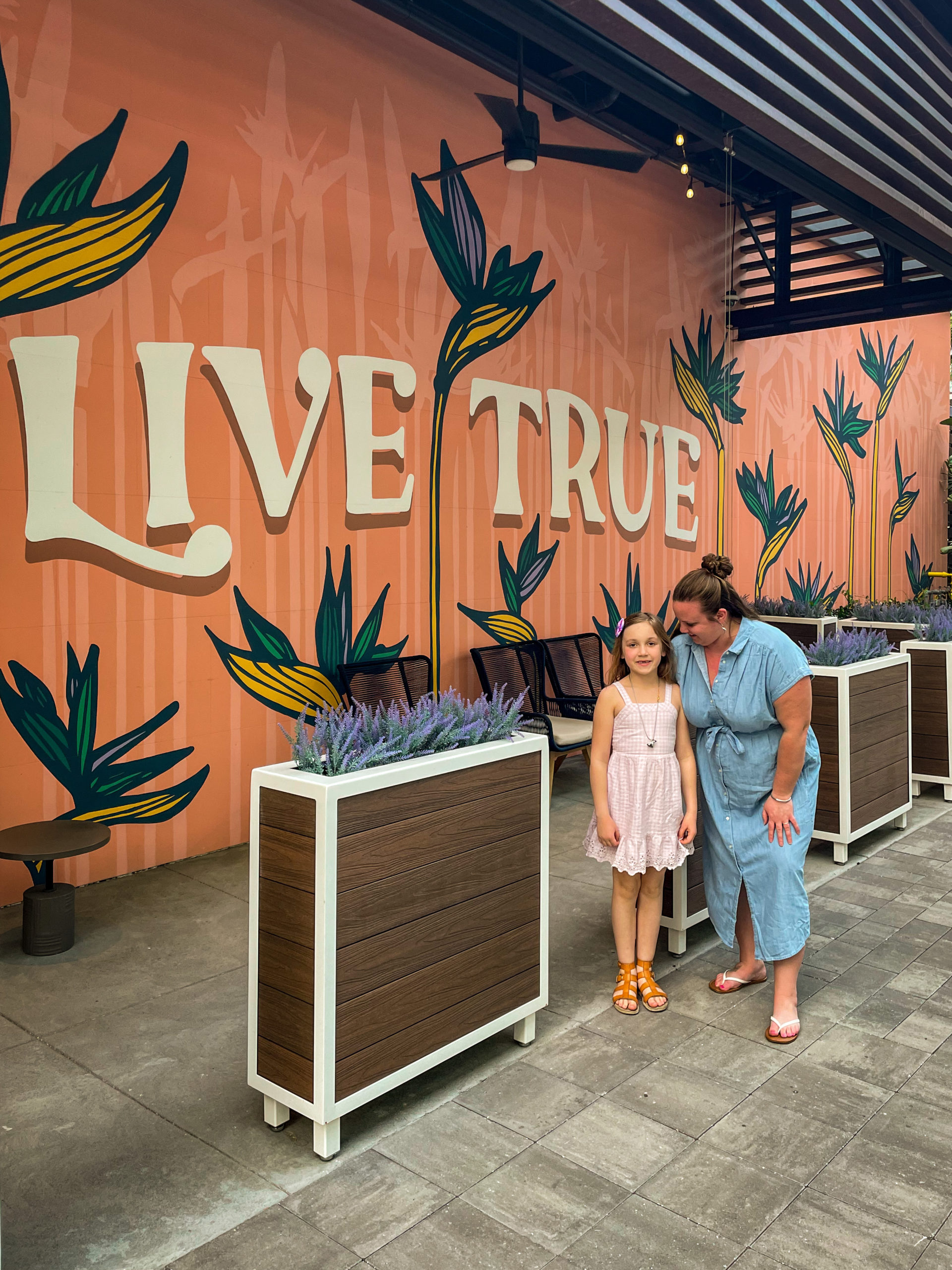 A young girl and her mom stand in front of a mural that says "Live True" in Midtown Tampa.