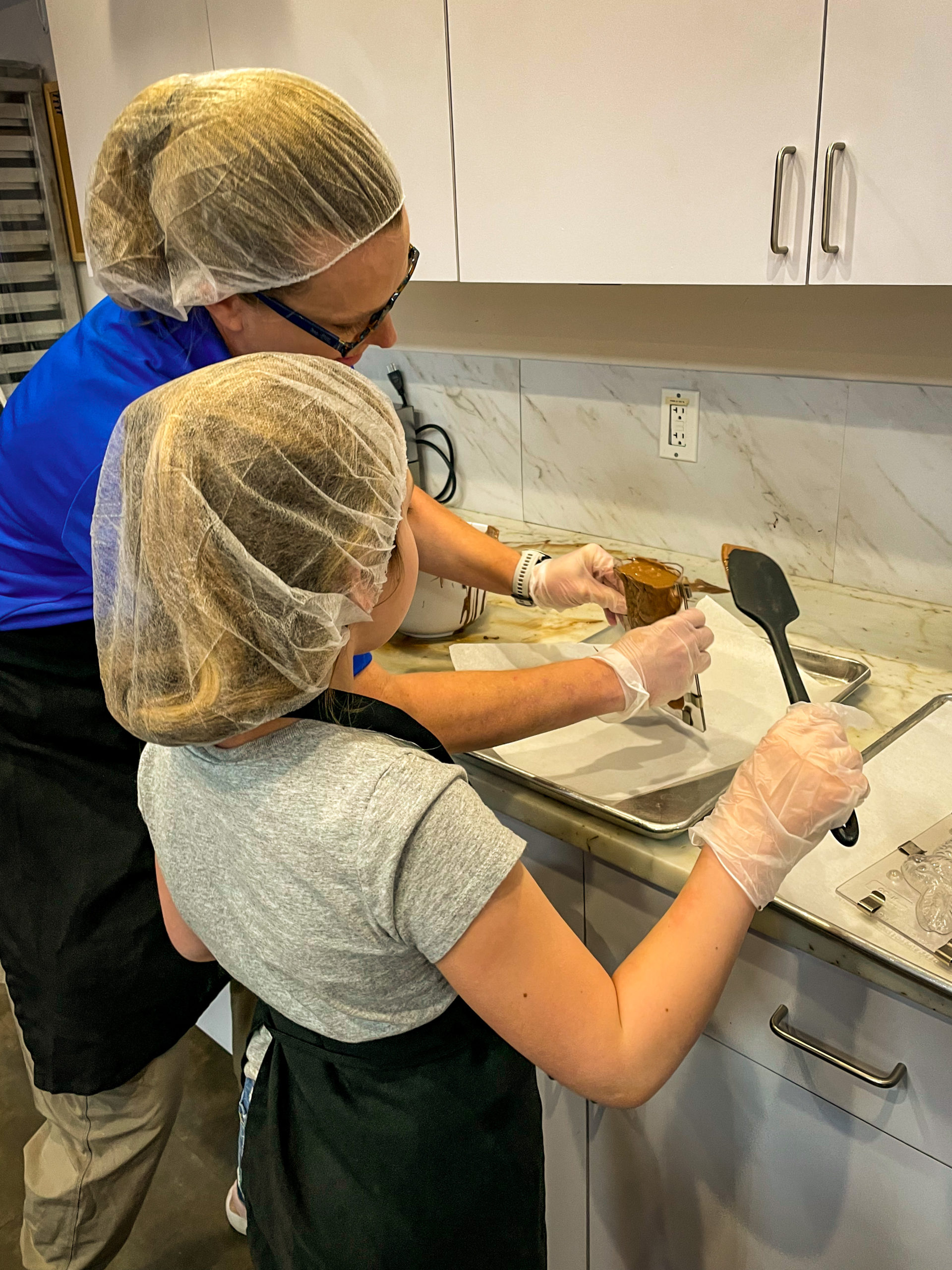 A young girl and the owner of Peterbrooke Chocolatier Tampa Downtown work together to fill a chocolate mold.