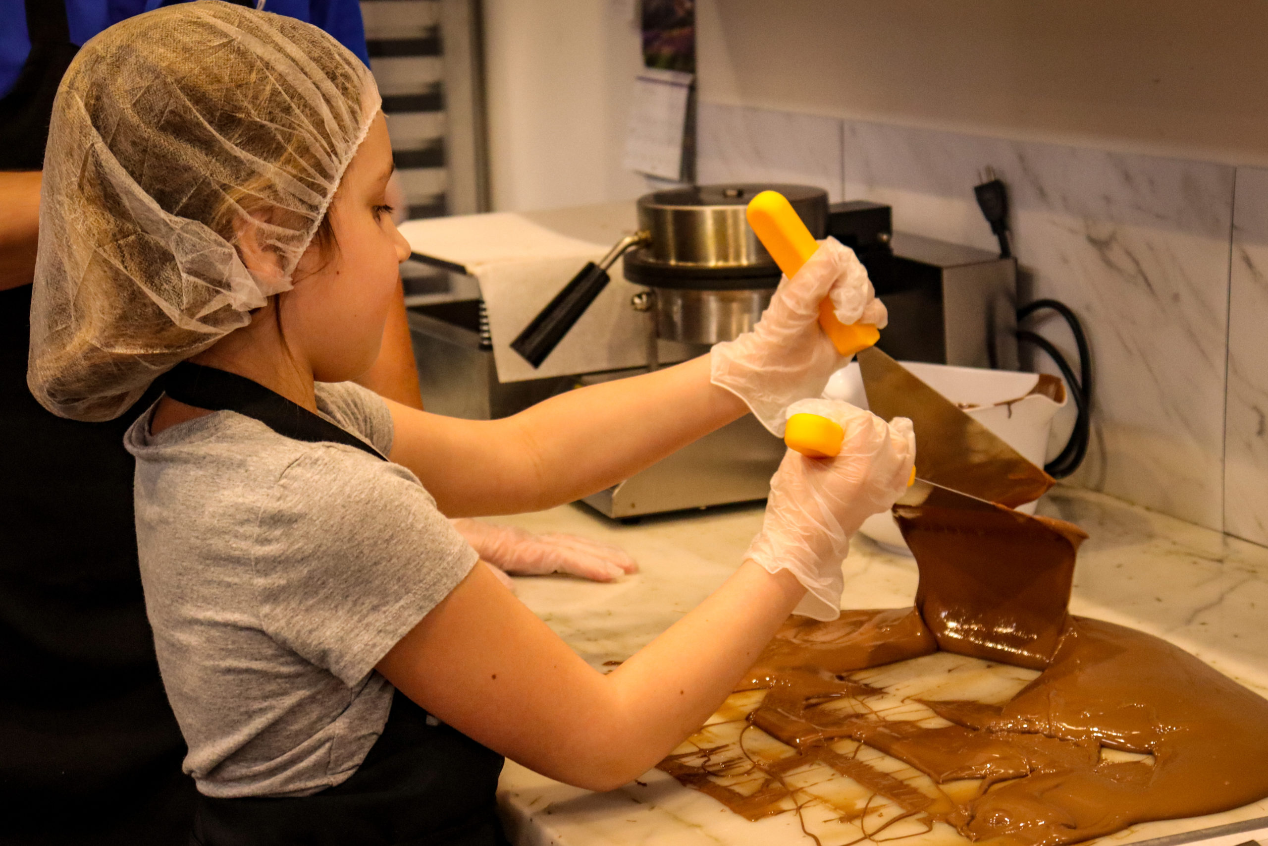 A young girl works to temper chocolate during a class at Peterbrooke Chocolatier Tampa Downtown.