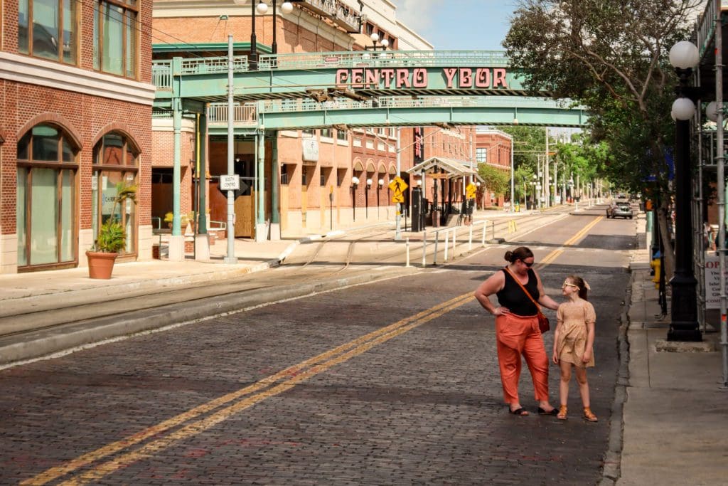 A mom and her young daughter stand together under the iconic Centro Ybor sign in Ybor City.