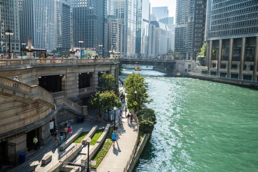 People meander the Riverwalk along the Chicago River on a sunny day.