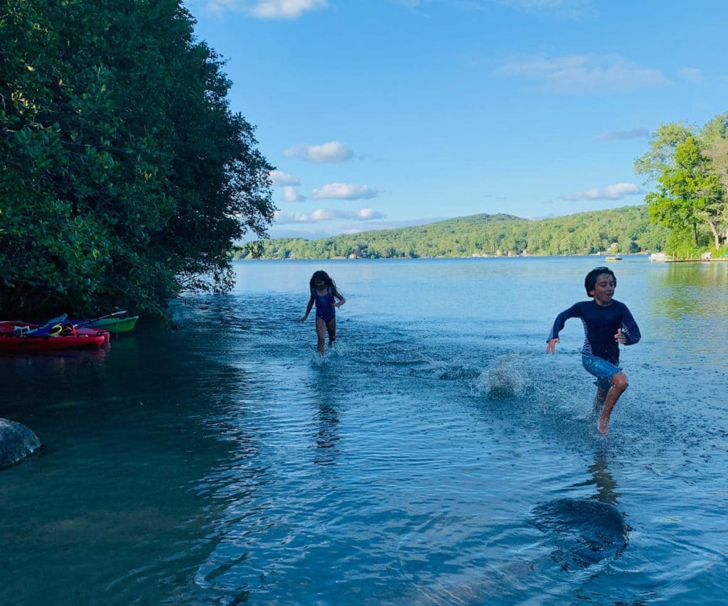 Two kids run through shallow waters along the shore of Highland Lake.