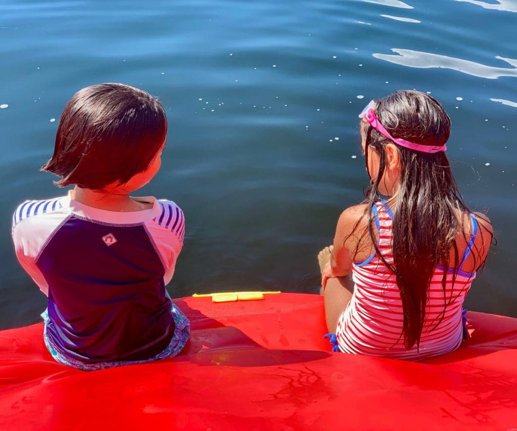 Two kids sit together at the edge of a lake inflatable while enjoying a sunny day at Highland Lake, one of the best lakes for a family vacation within 4 hours of NYC.
