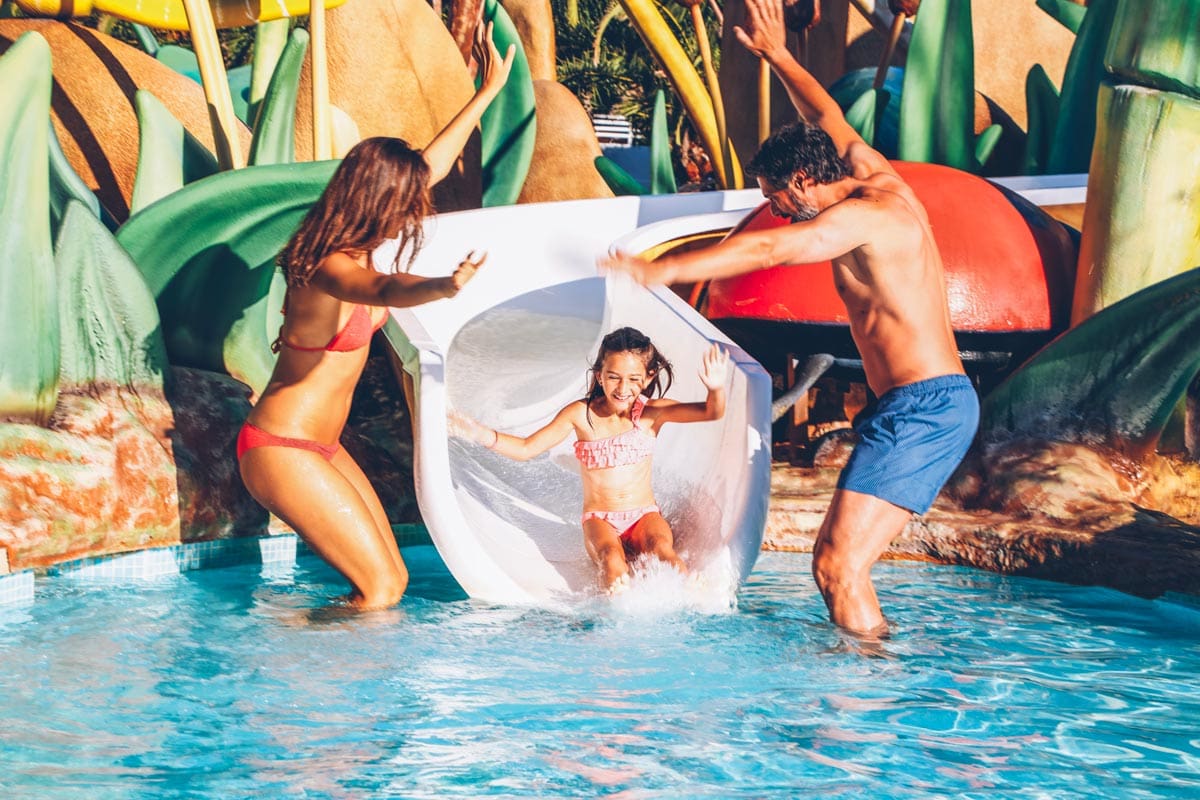 Two parents await their child, who is coming down a waterslide at Iberostar® Selection Albufera Park, one of the best all-inclusive hotels in Mallorca for families.