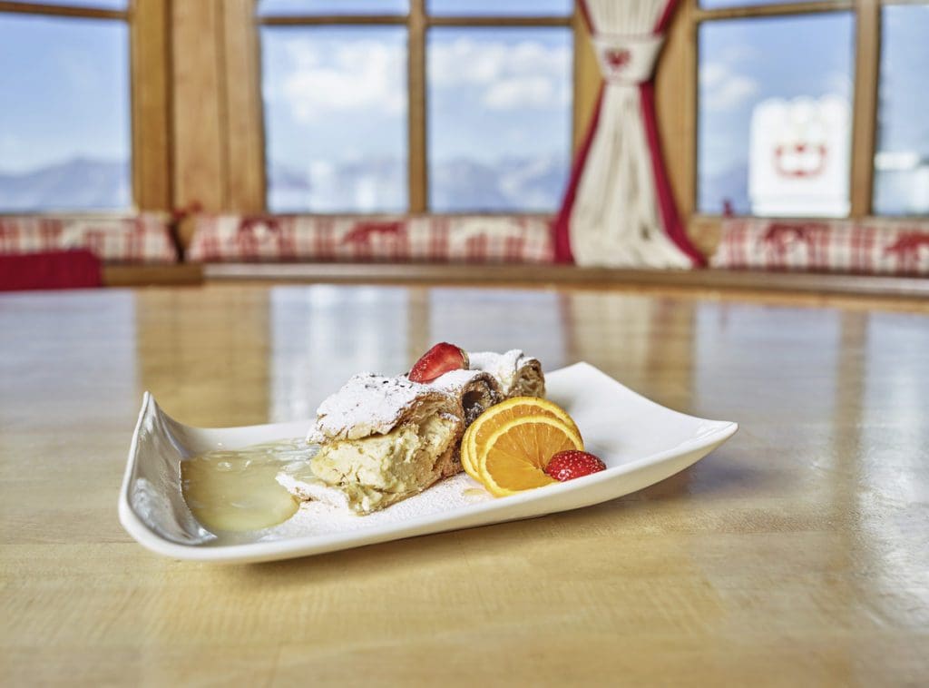 Fresh apple strudel on a plate, with a view of the mountains outside the windows.