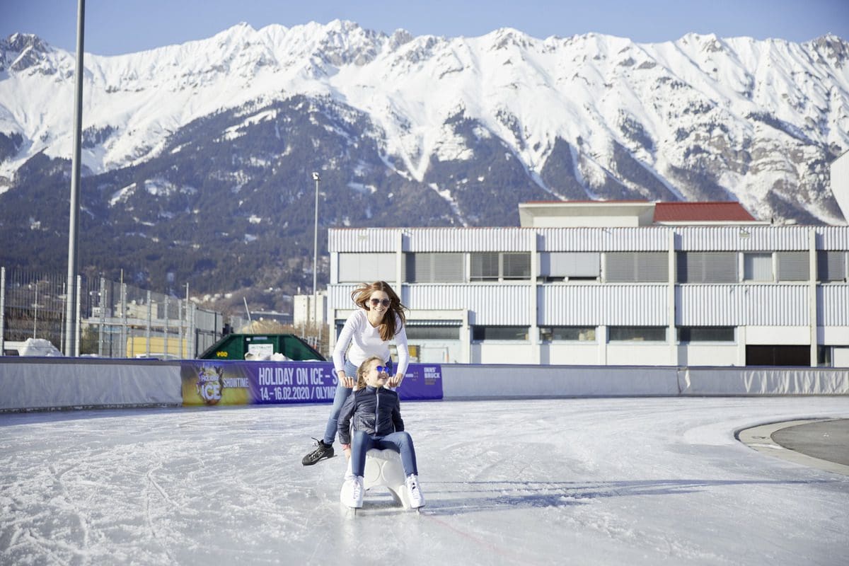 A mom pushes her young daughter on a chair around the ice rink, while skating around, in Innsbruck.