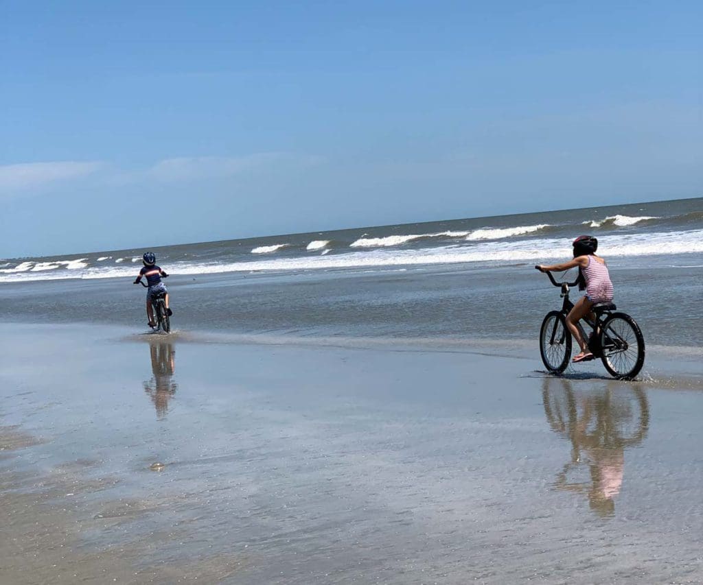 Two young kids riding bikes on a beach on Kiawah Island, one of the best beach towns on the East Coast with kids.