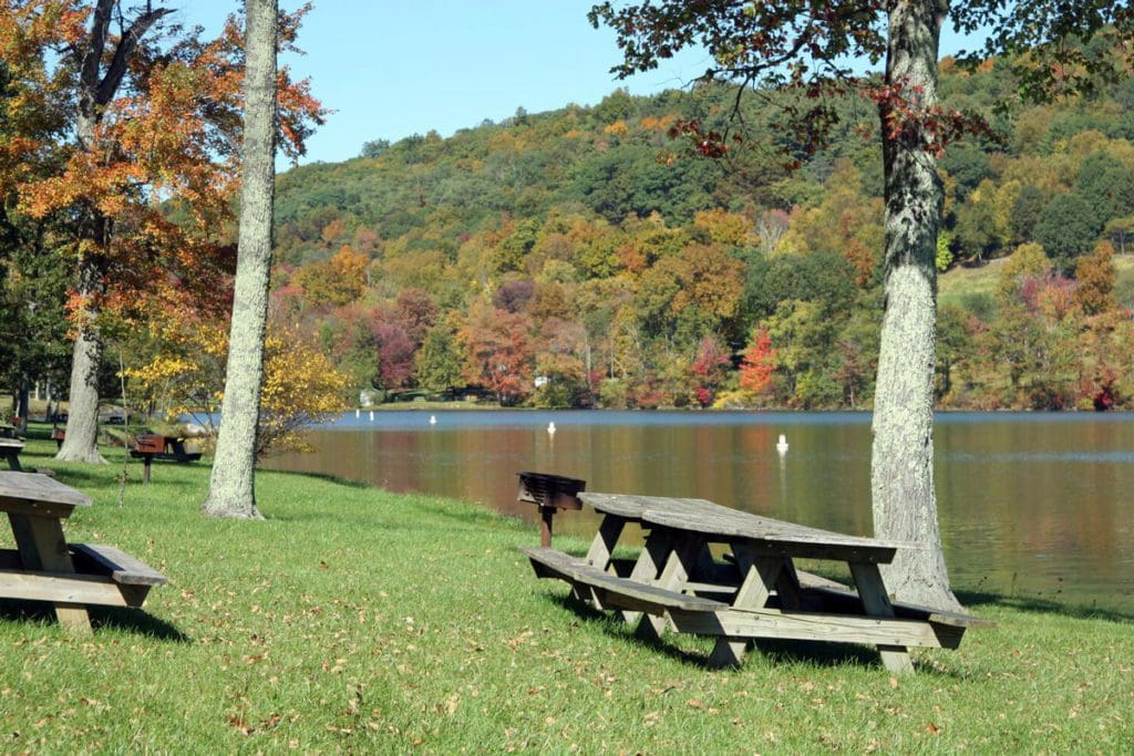 Several picnic tables on green grace near Lake Waramaug in the fall.