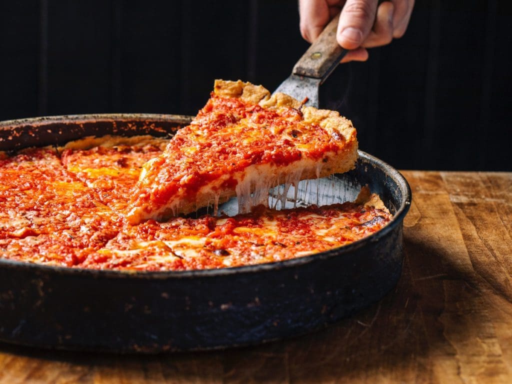 A hand uses a pizza serving utensil to pick up a slice of Chicago-style deep dish pizza from Lou Malnati's.