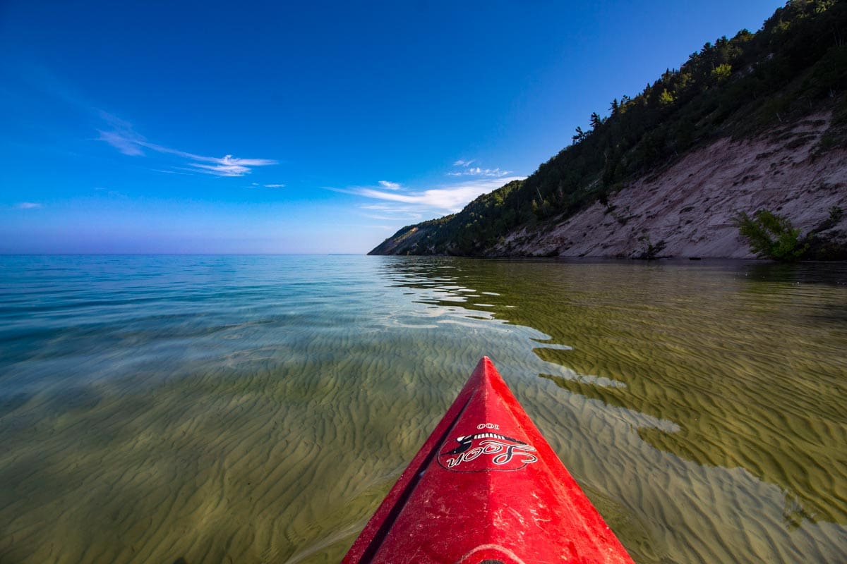 The nose of a red kayak maneuvers across Lake Michigan, one of the best lakes in Michigan for a family vacation.