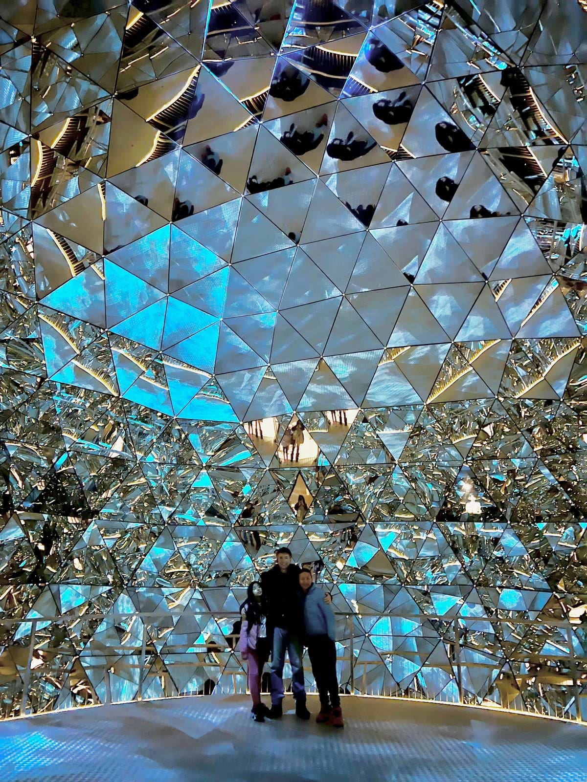 A dad and his two young kids stand together under a beautiful crystal display at Swarovski Kristallwelten, one of the best things to do near Innsbruck with kids this winter.