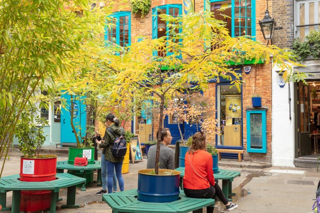 People sit on benches while enjoying urban greenery in the Covent Garden neighborhood of London.