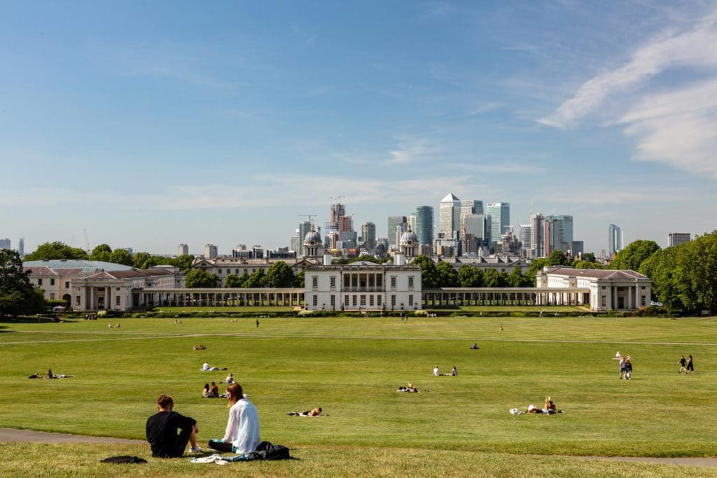 Several groups of people lounge on the lawn of the Naval College in London's Greenwich neighborhood on a sunny day.