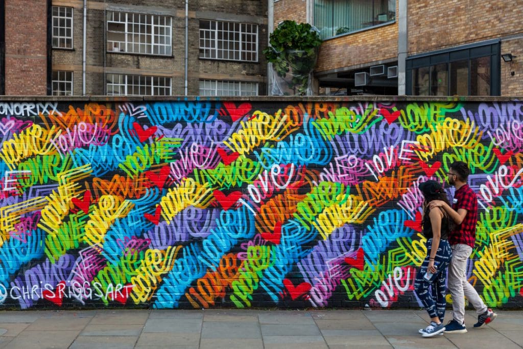 A couple walks by a vibrant mural in the Shoreditch neighborhood of London.