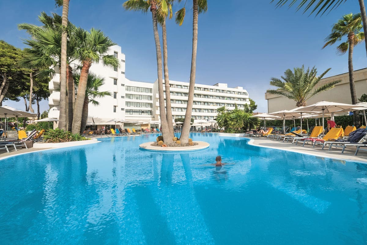 People swim in the beautiful outdoor pool, surrounded by swaying palm trees, at allsun Eden Playa.