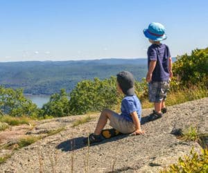 Two kids stand together looking out onto a scenic view from Bear Mountain.
