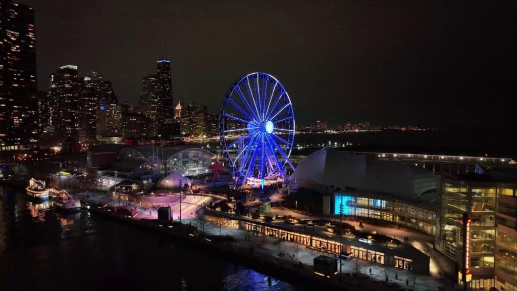 Navy Pier lit up at night with the Chicago skyline in the distance.