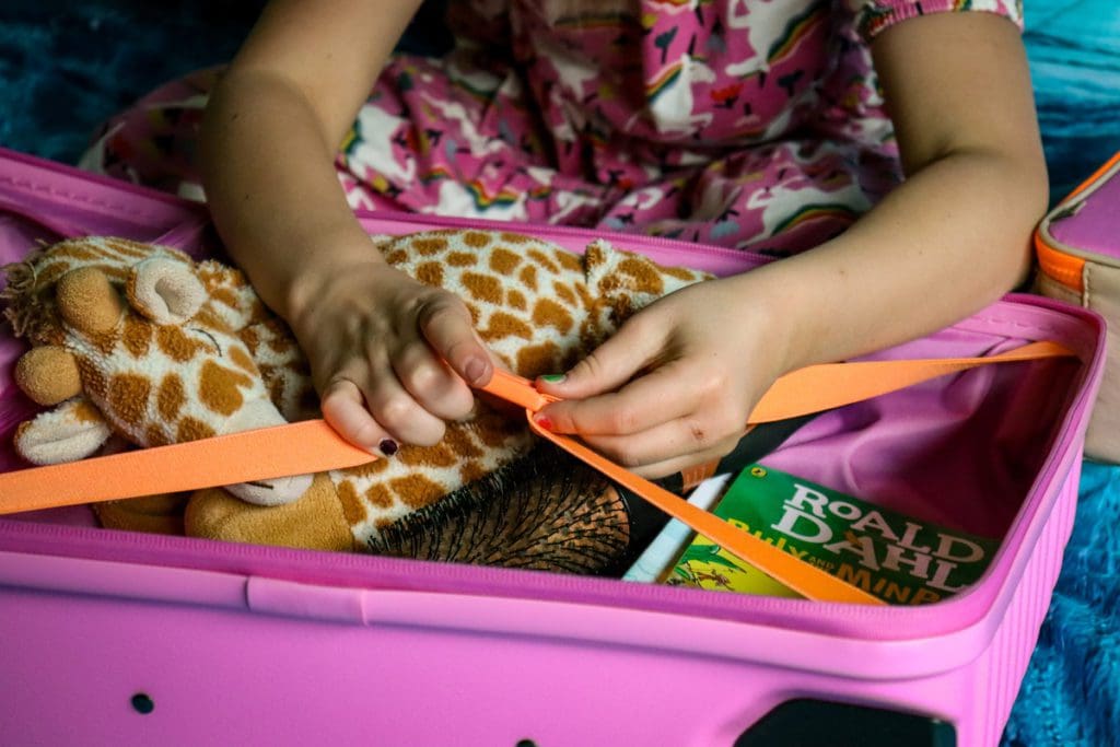 A young girl clips together an interior buckle of a suitcase to hold her belongings in place.