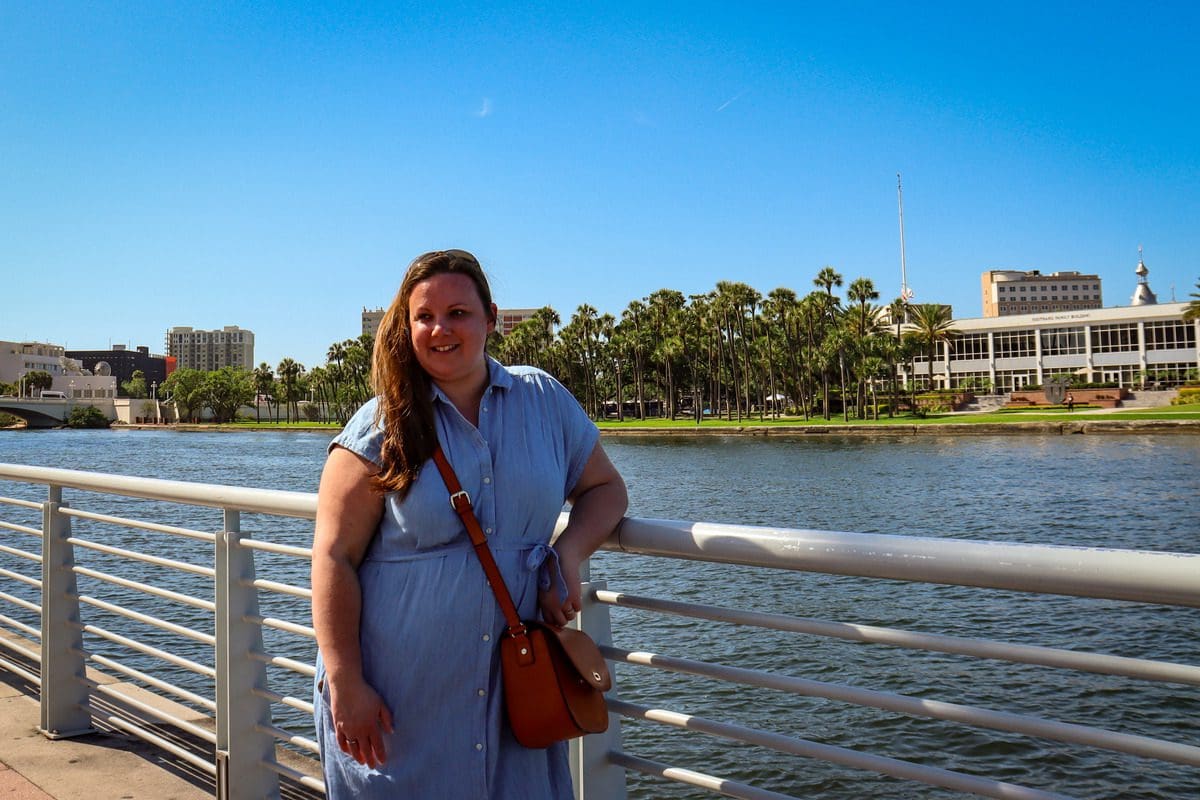 A woman stands along a railing with the Hillsborough River in the background along the Tampa Riverwalk.