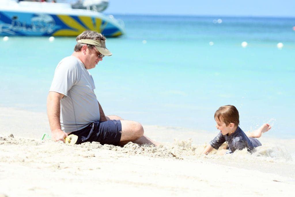 A dad and his young son play in the sand near the ocean, while staying at Beaches Negril, one of the best Jamaica all inclusive family resorts.