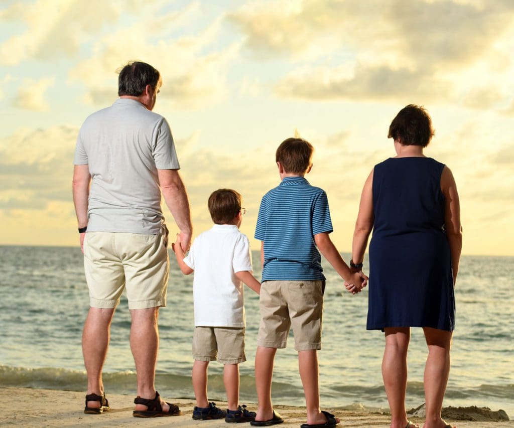 A family of four stands together looking out onto the ocean at dusk.