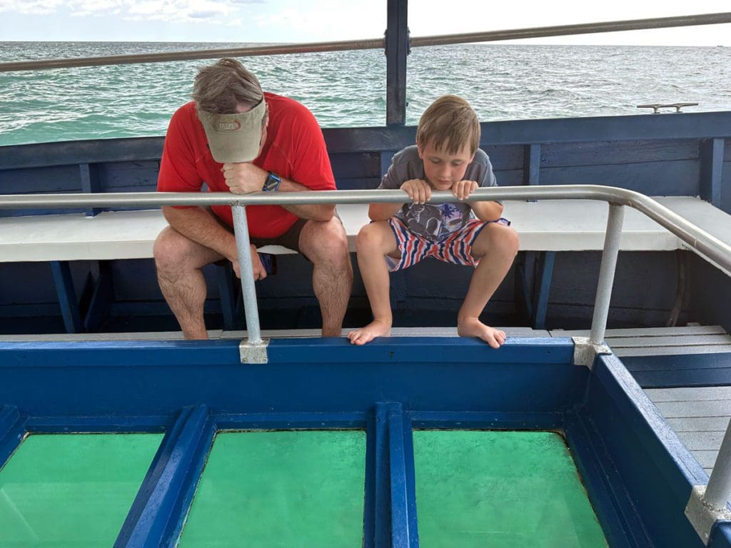 A dad and his young son look through the bottom of a glass-bottom boat while on a Beaches Negril tour for families.