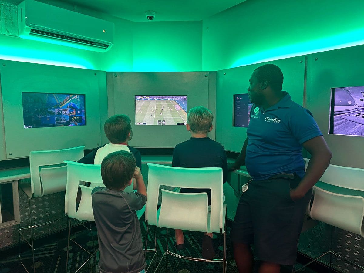 Three boys enjoy an Xbox game room with a staff member guiding them at Beaches Negril.