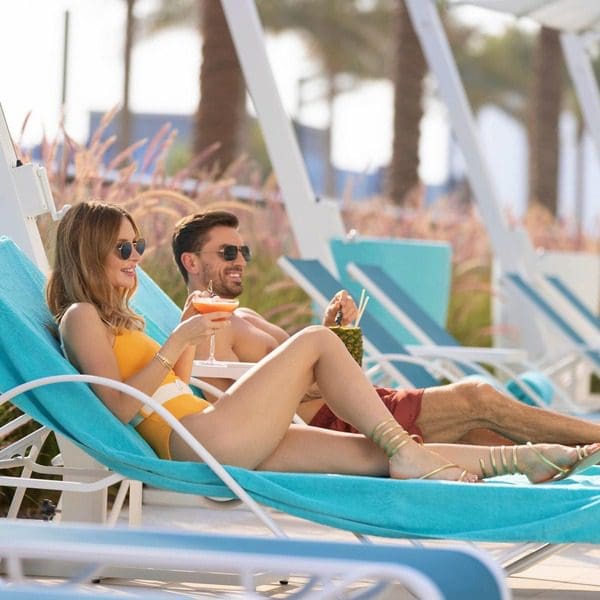 A couple enjoys drinks on beach loungers, while staying at Hilton Dubai Palm Jumeirah.