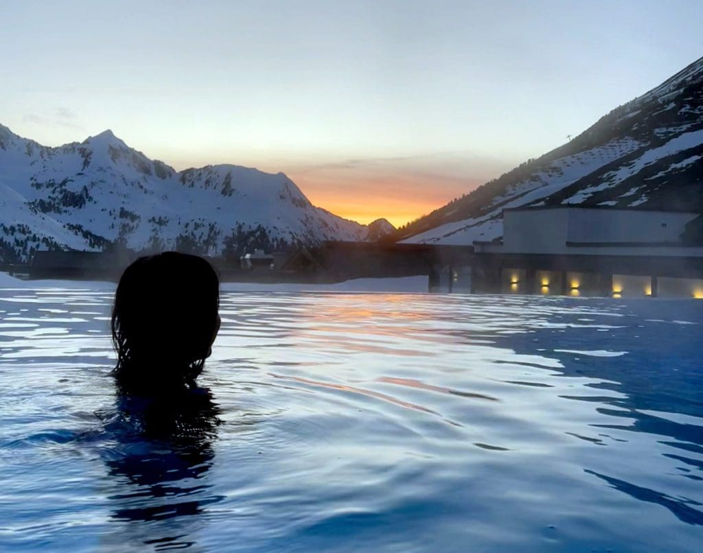 A woman swims in an adult-only pool with a lovely sunset in the distance over the Austrian Alps.