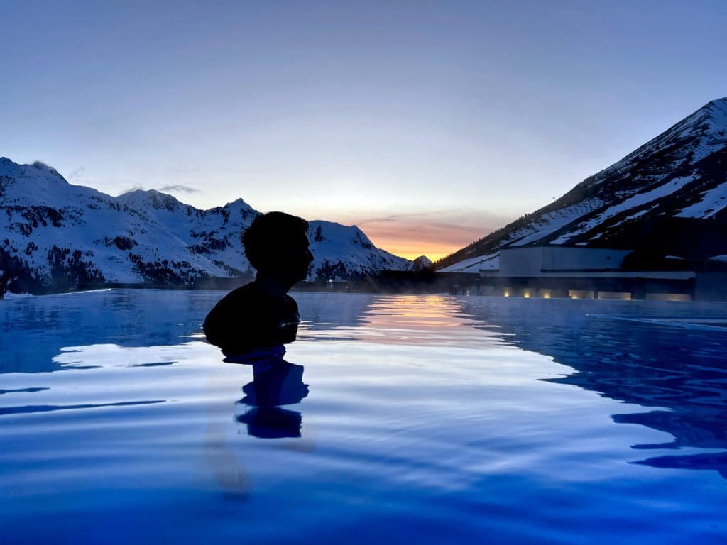 A man enjoys a sunset swim at the outdoor pool, just one of the many reasons why families adore Hotel Mooshaus for a family ski vacation in Austria.