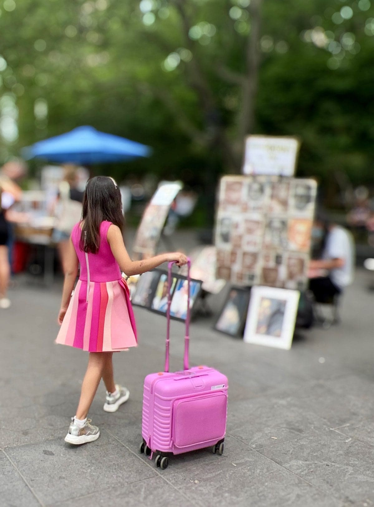 A tween girl walks through a NYC street fair with her luggage.