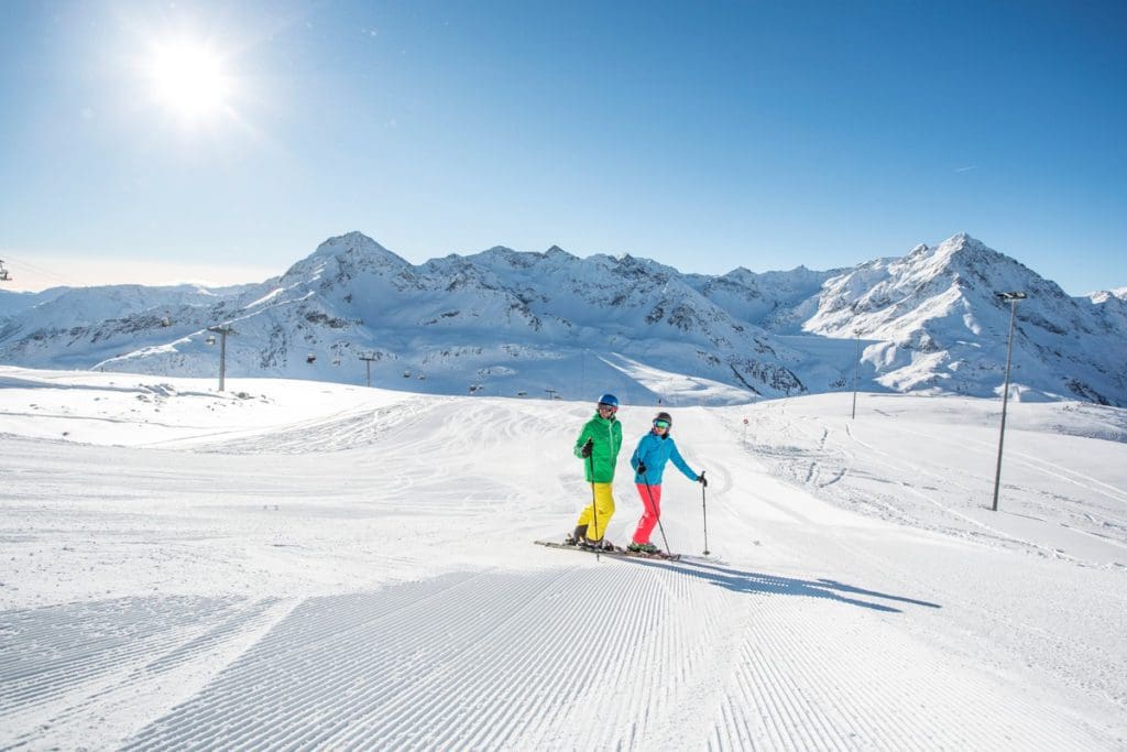 Two people in colorful ski outfits, skiing along a trail  in Austria.
